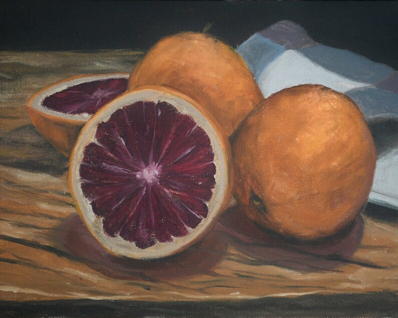 K&ouml;nnte beinhalten: Eine Stillleben-Malerei mit drei Orangen auf einem Holztisch. Eine Orange ist halbiert und zeigt ein tiefrotes Fruchtfleisch. Die Orangen sind auf einem wei&szlig;en Tuch angeordnet.
