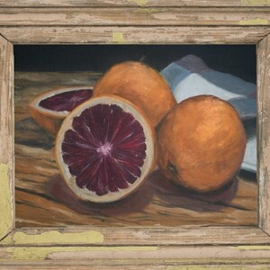 K&ouml;nnte beinhalten: Ein Stillleben mit drei Orangen, von denen zwei halbiert sind und ihr tiefes rotes Fruchtfleisch zeigen. Die Orangen sind auf einem Holztisch mit einem wei&szlig;en Tuch im Hintergrund angeordnet.