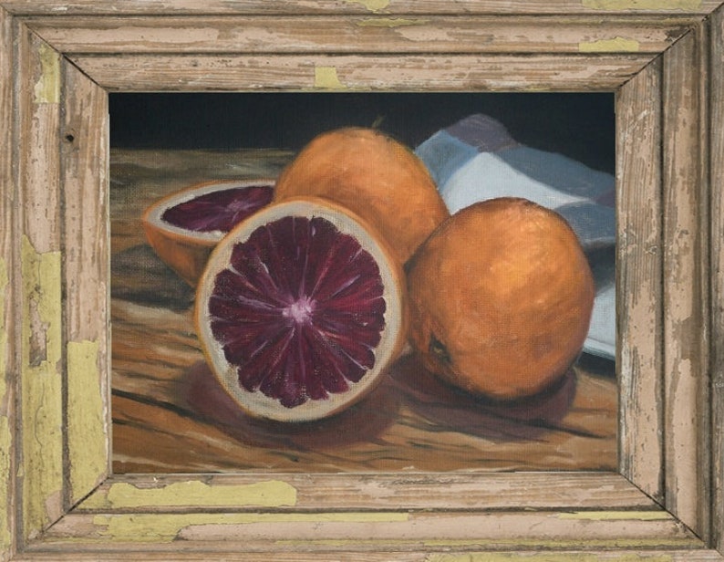 K&ouml;nnte beinhalten: Ein Stillleben mit drei Orangen, von denen zwei halbiert sind und ihr tiefes rotes Fruchtfleisch zeigen. Die Orangen sind auf einem Holztisch mit einem wei&szlig;en Tuch im Hintergrund angeordnet.