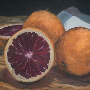 K&ouml;nnte beinhalten: Drei Orangen, eine davon halbiert, auf einer Holzoberfl&auml;che. Die geschnittene Orange zeigt ein tiefrotes Fruchtfleisch.