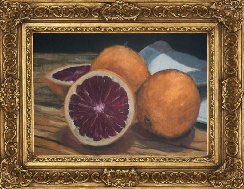 K&ouml;nnte beinhalten: Ein Stillleben mit drei Orangen auf einem Holztisch. Eine Orange ist halbiert und zeigt ein tiefrotes Fruchtfleisch. Die Orangen sind in einer Gruppe angeordnet, wobei die geschnittene Orange in der Mitte liegt.