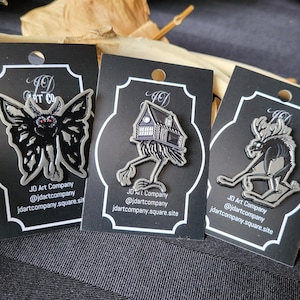 Peut inclure: Trois épingles en émail représentant un papillon de nuit noir, une maison sur pilotis et un élan. Chaque épingle est en argent et est présentée sur une carte noire avec le texte "JD Art Company @jdartcompany jdartcompany.square.site".