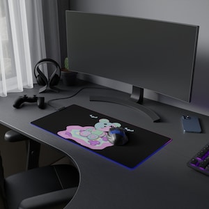 May include: A black gaming mouse pad with a colorful cartoon bear design and bats. The mouse pad is lit with a blue and purple glow. A black gaming mouse is on the mouse pad.