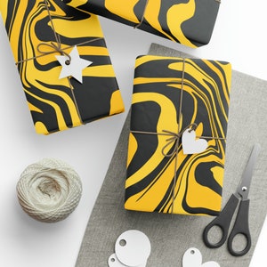 May include: Three gift boxes wrapped in black and yellow marbled paper with twine and white paper tags. The boxes are on a white surface with a gray fabric surface in the background.