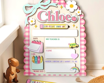 May include: A personalized wooden sign for the first and last day of school, featuring the name "Chloe" in pink. The sign has a pink and white checkered background, a bow, flowers, and space to write details about the school year.