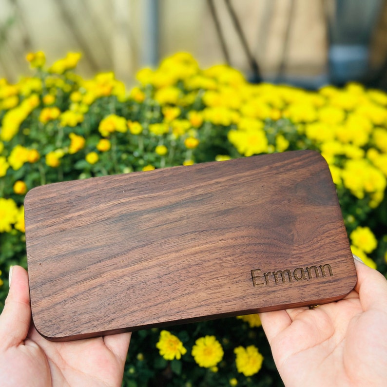 Pu&ograve; includere: Un vassoio rettangolare in legno con una finitura in legno a grana marrone scuro. Il vassoio ha il nome "Ermann" inciso sulla superficie.
