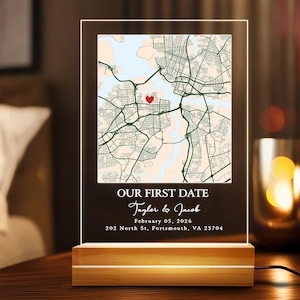May include: A personalized acrylic map night light with a wooden base. The map features a red heart marking a location. Text reads "OUR FIRST DATE" with names and a date. The base is illuminated.