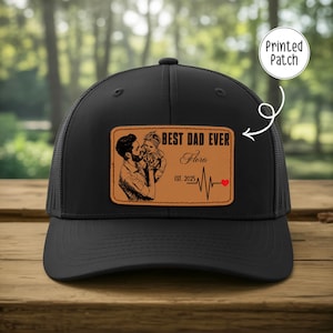 May include: Black trucker hat with a brown leather patch. The patch features a graphic of a father holding a baby, the text "BEST DAD EVER", the name "Flora", the year "EST. 2025", and a heartbeat graphic with a red heart.
