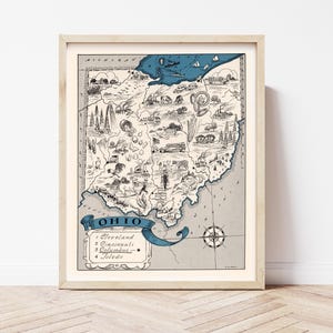 May include: Framed vintage-style map of Ohio, featuring detailed illustrations of landmarks and cities. The map is in black and white with blue accents, including a banner that reads "Ohio" and lists major cities. The frame is a light wood color.
