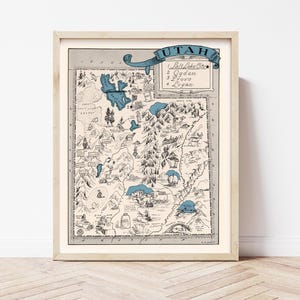 May include: Framed vintage-style map of Utah, with a detailed illustration and blue accents. The map highlights major cities including Salt Lake City, Ogden, Provo, and Logan. The artwork is encased in a light-coloured wooden frame.
