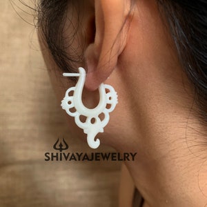 Puede incluir: Pendientes de aro de hueso blanco con un diseño delicado e intrincado. Los pendientes tienen forma de herradura con un patrón floral decorativo.
