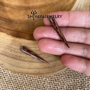 May include: Two brown and black wood-like pointed earrings. The earrings are approximately 5 cm long and have a slightly twisted design.