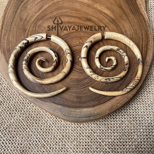 May include: A pair of wooden spiral earrings with a natural wood finish and black swirl patterns. The earrings are displayed on a wooden surface.