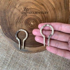 May include: Two wooden ear gauges with a black and white marbled pattern. The gauges are shaped like a teardrop with a rounded top and a pointed bottom.