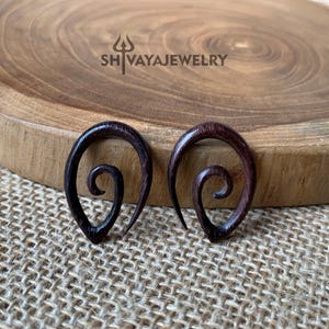 May include: A pair of dark brown wooden earrings with a spiral design. The earrings are shaped like a teardrop and have a smooth, polished finish.