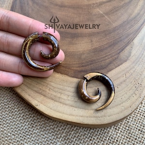 May include: Two brown and gold spiral wood earrings. The earrings are made of wood and have a spiral design. The earrings are on a wooden surface.