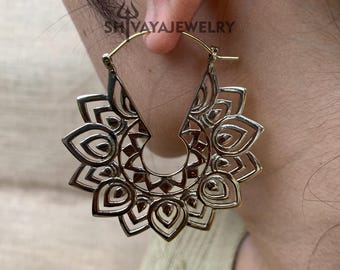 May include: Gold-toned metal hoop earrings with a detailed mandala design. The earrings are large and have a delicate, intricate pattern.