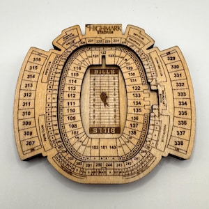 Può includere: Una mappa in legno dello stadio Highmark, sede dei Bills. La mappa è intagliata al laser, mostrando le sezioni dei posti a sedere, etichettate con numeri e testo. Il logo dei Bills è visibile al centro del campo.