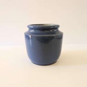 May include: A navy blue ceramic jar with a wide opening and a slightly rounded body. The jar has a glossy finish and a simple, classic design. The jar is suitable for kitchen or home decor.