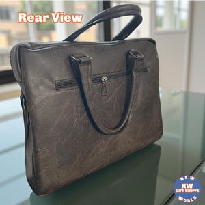 The back of a dark brown vegan leather briefcase shows a zippered pocket and two handles, resting on a reflective surface.