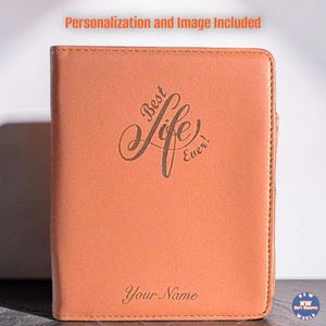 May include: A peach-colored rectangular passport holder or notebook cover featuring the engraved text Best Life Ever! in a cursive script, with the placeholder text Your Name engraved at the bottom. The top text reads Personalization and Image Included.