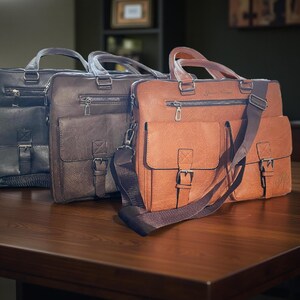 Three vegan leather briefcases, in black, dark brown, and brown, are arranged diagonally on a wooden table.