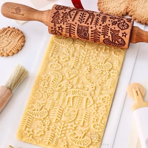 May include: A wooden rolling pin with a Christmas-themed design is used to roll out cookie dough. The dough is imprinted with a pattern of trees, stars, reindeer, and other festive elements. The rolling pin has the words "Cookie Cutter" printed on it.