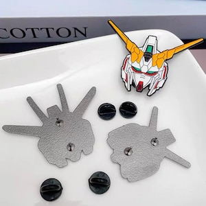 May include: Three silver metal enamel pins featuring a robot head, a hand with three fingers, and a hand with two fingers. The pins are on a white surface with four black metal pin backs.
