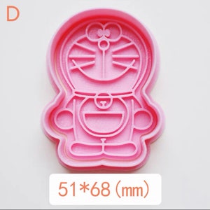 May include: Pink plastic cookie cutter shaped like a cartoon character with a round head, big eyes, and a smile. The cutter measures 51 by 68 millimetres.
