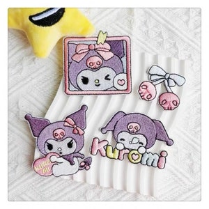 May include: Five embroidered iron-on patches featuring a cartoon character with a skull and bow. The patches are purple, pink, and white. One patch says "Kuromi" in pink and white letters.