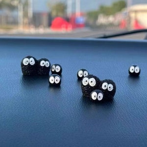 May include: A collection of small, black, fuzzy, round figurines with white eyes. The figurines are arranged on a dark blue surface.