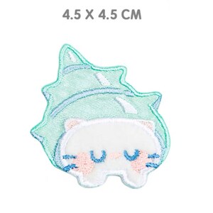 Könnte beinhalten: Gestickter Aufnäher mit einem weißen Cartoon-Tier mit geschlossenen blauen Augen und rosa Wangen, umgeben von einer hellgrünen blattartigen Form. Misst 4,5 x 4,5 cm.
