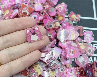 May include: A large assortment of pink and clear resin flatback embellishments featuring cartoon bears, stars, and other designs.
