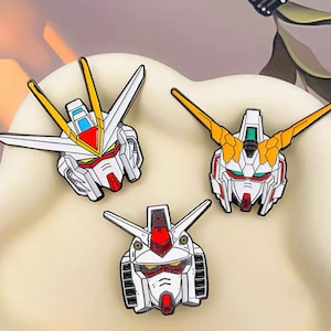 May include: Three enamel pins featuring the heads of different robots from the anime series "Gundam". The pins are white, red, yellow, and blue.