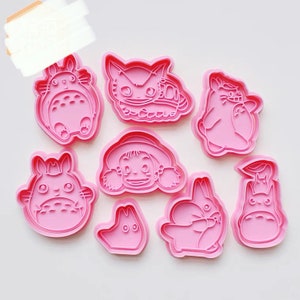 Pode incluir: Um conjunto de oito cortadores de biscoitos de plástico rosa com personagens do filme de animação Meu Vizinho Totoro. Os cortadores têm a forma de Totoro, o ônibus-gato e outros personagens do filme.