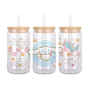 Puede incluir: Conjunto de tres vasos de vidrio transparente con tapas de bambú y pajitas. Cada vaso presenta una ilustración diferente del personaje Cinnamoroll de la franquicia Sanrio. Los vasos están decorados con un patrón de cuadros rosa y blanco, margaritas blancas y el texto "Cinnamoroll Cafe".
