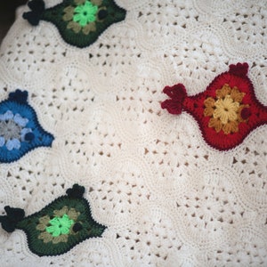 Puede incluir: Una manta blanca de ganchillo con p&aacute;jaros de ganchillo de colores. Los p&aacute;jaros son en tonos de rojo, azul, verde y amarillo.