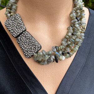 May include: A multi-strand necklace made of grey and black stones with a large, black, crystal-encrusted bow accent.