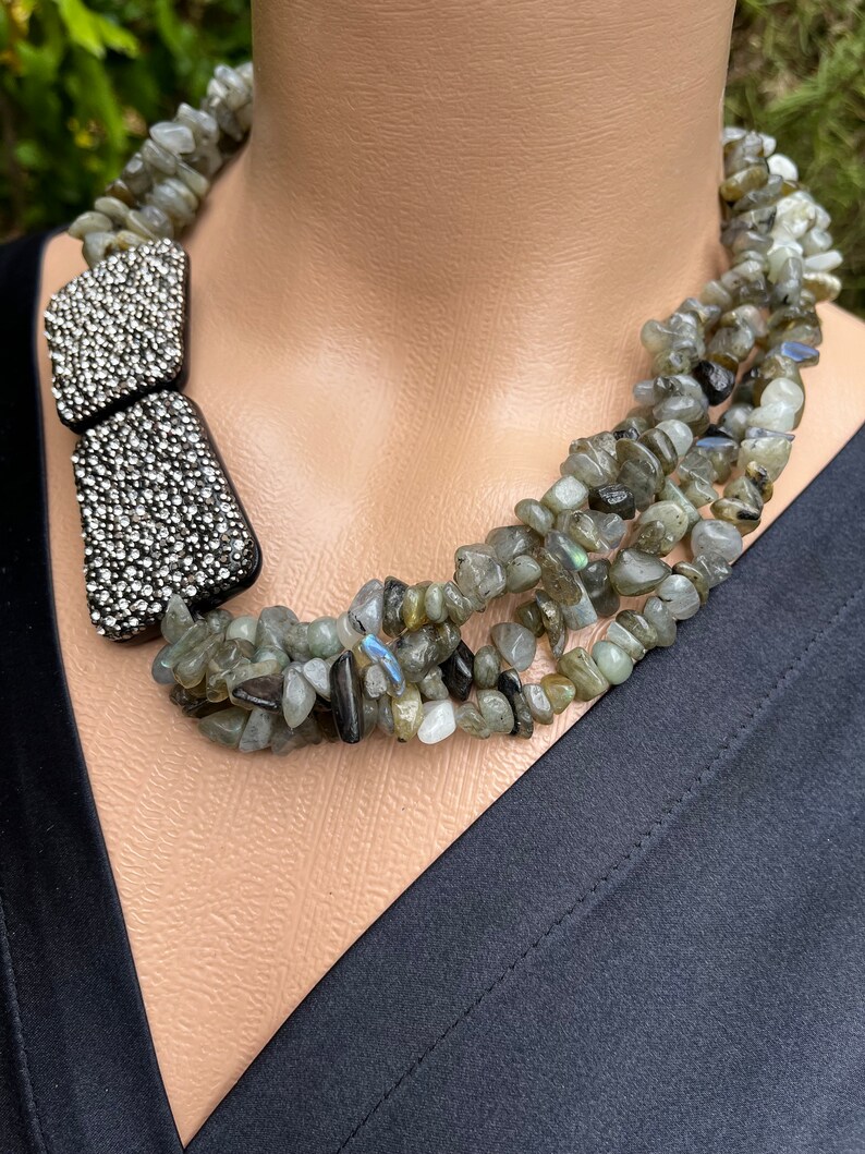 May include: A multi-strand necklace made of grey and green gemstone beads with a silver rhinestone accent.