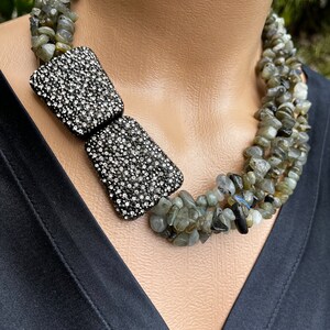 May include: A multi-strand necklace made of green and gray stones with a large, silver, rhinestone bow pendant.