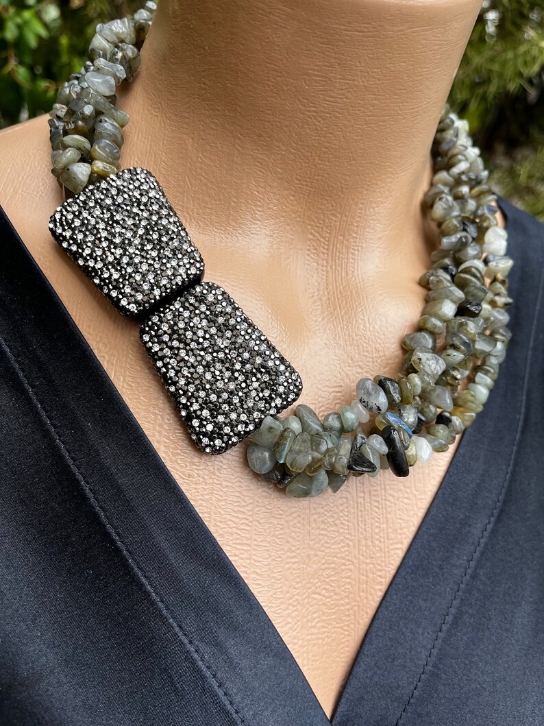 May include: A multi-strand necklace made of green and gray stones with a large, silver, rhinestone bow pendant.