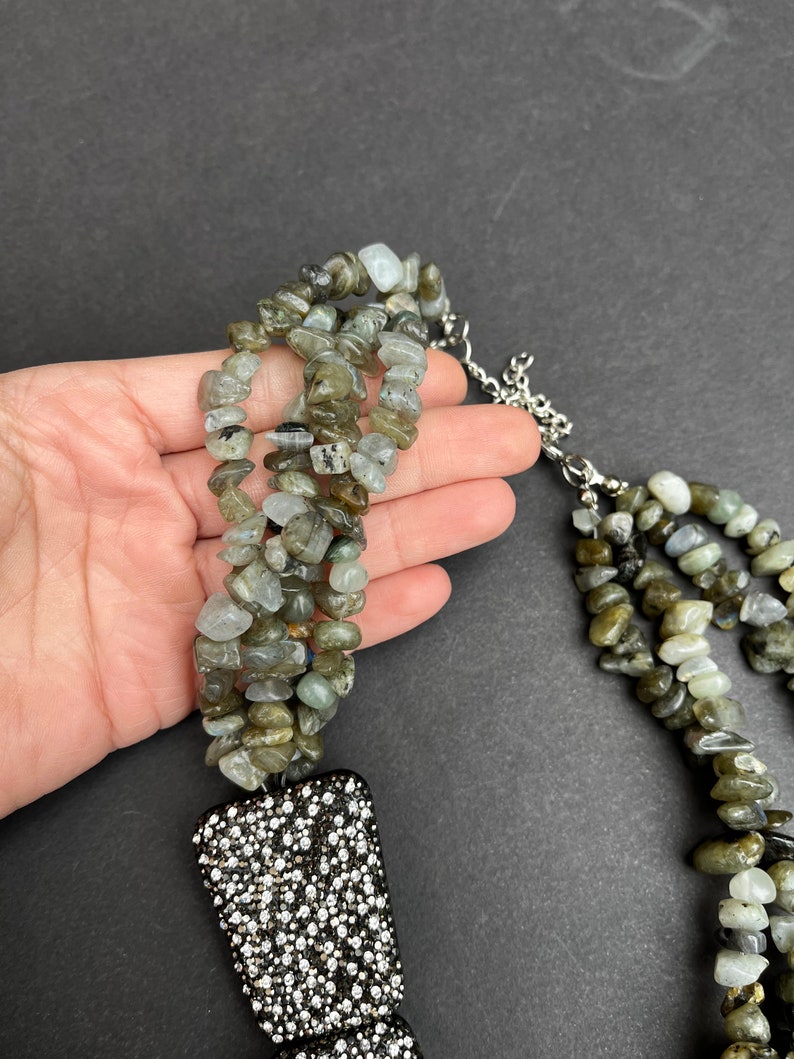 May include: A multi-strand necklace made of green and gray stones with a large, black, rhinestone-encrusted pendant.