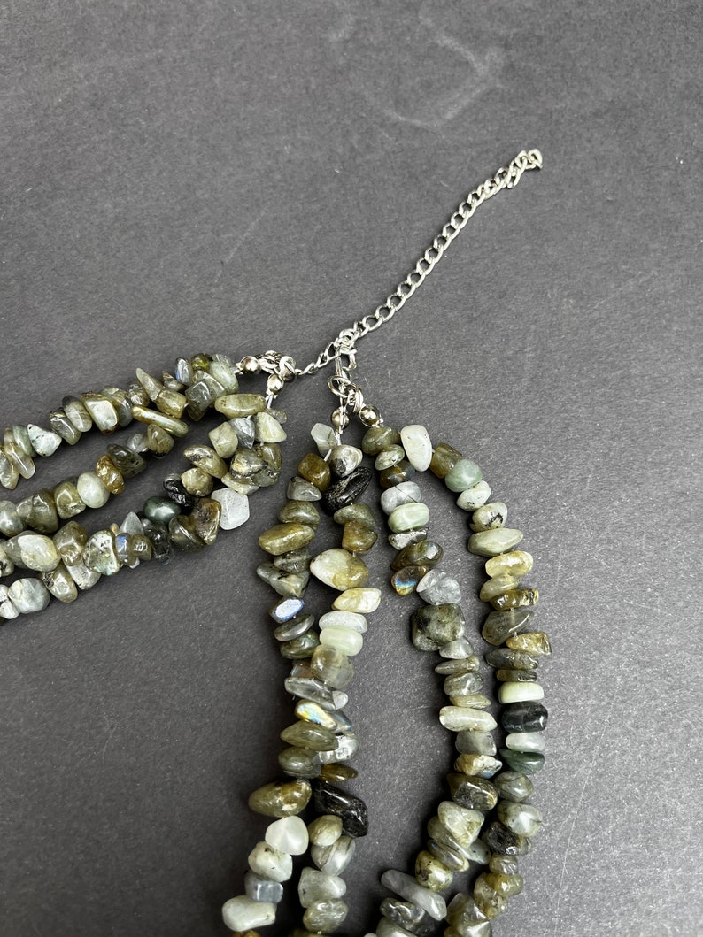 May include: A multi-strand necklace made of grey and green labradorite stones. The necklace has a silver chain extender.