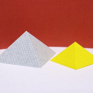 Peut inclure: Deux pyramides, l'une grise et l'autre jaune, sont posées sur une surface blanche. La pyramide grise est plus grande que la pyramide jaune.