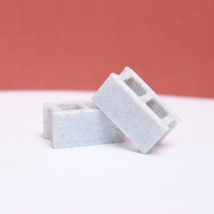 Pode incluir: Dois pequenos blocos de concreto branco com textura áspera. Os blocos estão empilhados um em cima do outro.