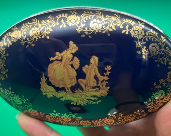 Puede incluir: Caja de baratijas ovalada Limoges azul marino con un borde floral dorado y una ilustración dorada de una pareja con ropa de época. La palabra "Limoges" está impresa en oro.