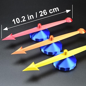 May include: Three colorful arrow-shaped objects, each 10.2 inches (26 cm) long, rest on blue bases. The arrows are red, orange, and yellow, with matching colored pegs. The objects are likely decorative or functional, possibly for a clock or gauge.