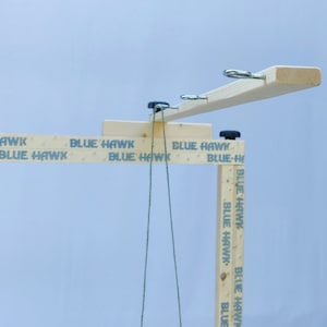 May include: A wooden game with a horizontal bar and strings hanging down. The bar has metal rings attached to it. The wooden posts have the text "BLUE HAWK" printed on them.