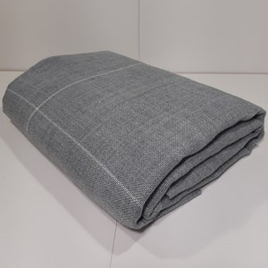 May include: A folded gray blanket with a subtle grid pattern. The blanket is a solid gray color with a white grid design. The fabric appears to be a woven material, and the blanket is neatly folded, showcasing its texture and construction.