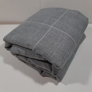 May include: Folded gray fabric with a white grid pattern. The fabric is a medium gray color and appears to be a woven material. The grid lines are thin and evenly spaced, creating a subtle design.